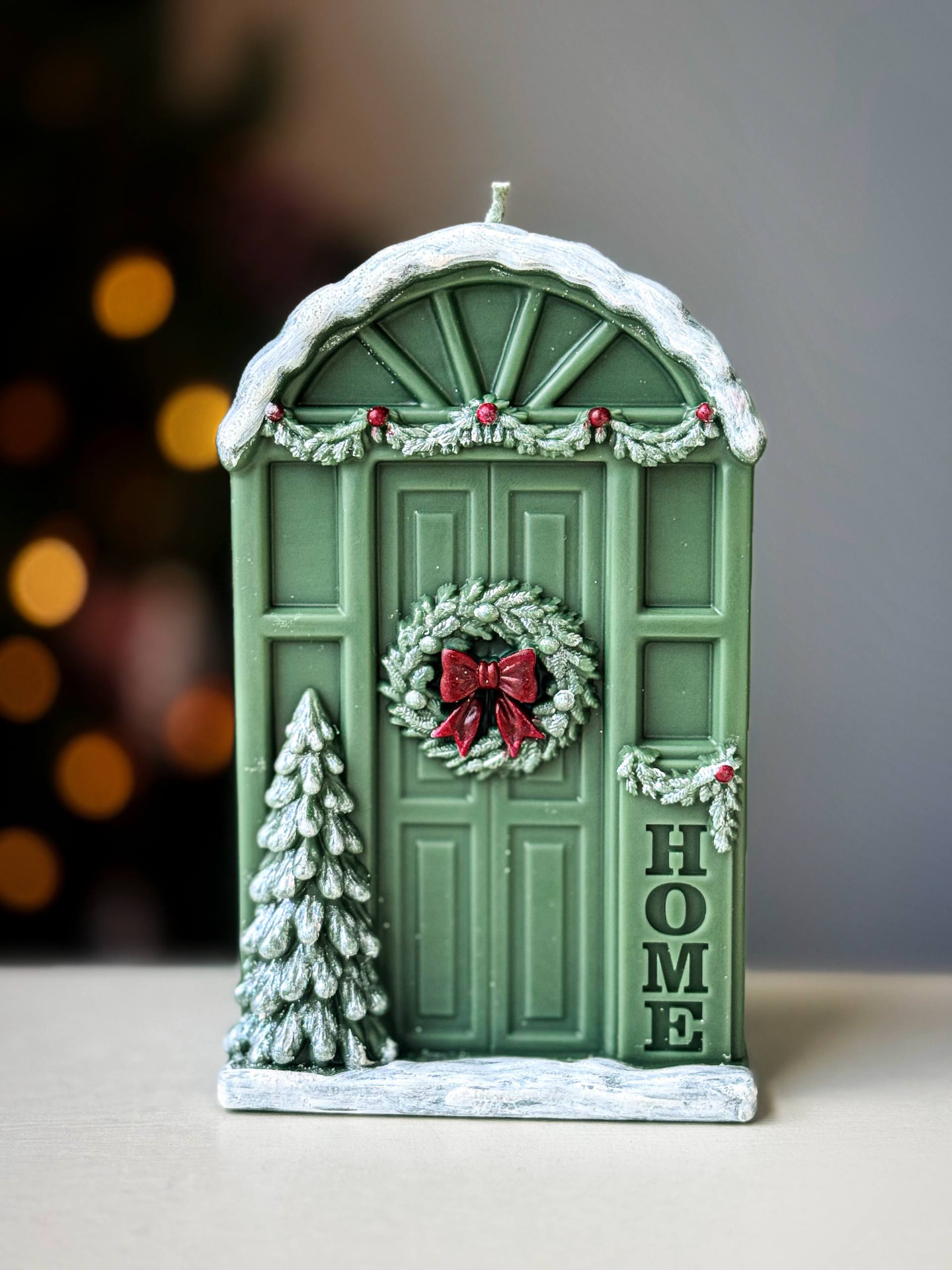 Green Christmas Door candle with a wreath and red bow, snowy arch, garland with berries, a frosted tree and a HOME sign